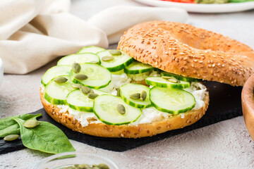 Ready-to-eat bagel stuffed with feta, cucumber and pumpkin seeds and spinach leaves on a slate board. Light Vitamin Healthy Snack. Close-up