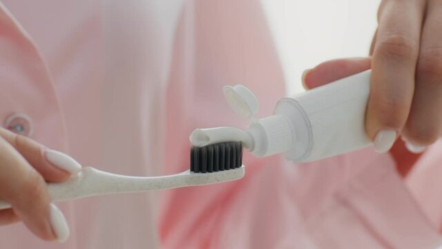 Unrecognizable woman squeezing white toothpaste from a tube onto toothbrush
