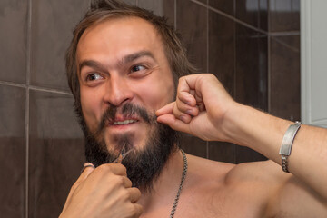 The man holds himself by the beard with two fingers by the mustache and holds scissors near the...