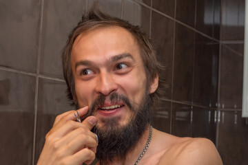 A man strokes his mustache with his fingers holding a pair of manicure scissors in his hand