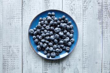 Blueberries on blue plate on wooden table top view