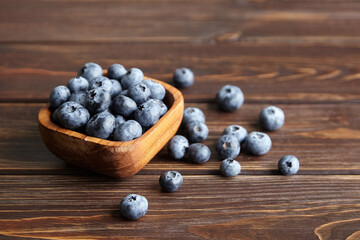 Bowl with fresh blueberries scattered on wooden table