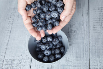 A handful of blueberries and bowl on wooden background