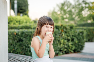 Fototapeta premium girl in a light dress eats popsicle ice cream in a city park. Children's rest in the summer.