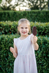 girl in a light dress eats popsicle ice cream in a city park. Children's rest in the summer.