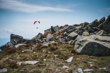 Naklejka premium Paraglider silhouette flying over mountains in beautiful warm summer day. Active wallpapers full of freedom. Paraglider flying over a scenic mountainous landscape.