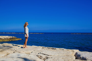 A beautiful girl stands on the rocky shore of the Mediterranean Sea Cyprus.Cheerful girl rests on the sea