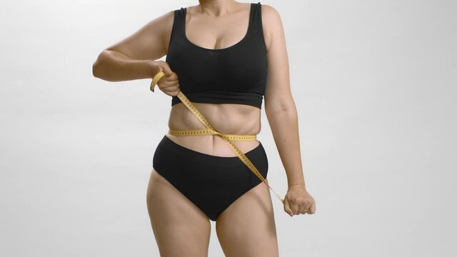 Obesity problems. Fat female measuring tightens up measuring tape around her body. Insecure, needs healthy weight loss diet. Disappointed. Still shot of body parts high quality video. 