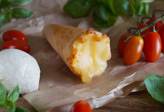 The pizza cone lies on the paper. This is a pizza with tomatoes and mazzarella cheese. .This is pizza Margarita