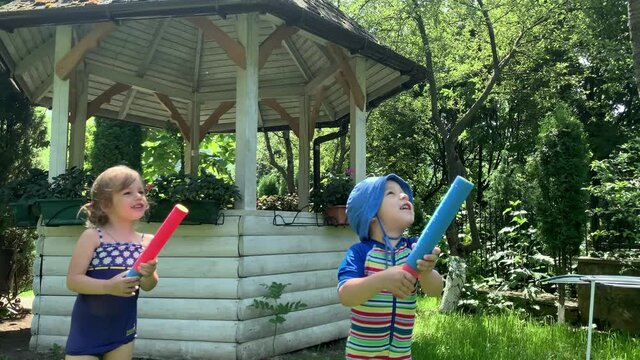 Cute Happy Kid Little Preschool Baby Girl and Boy Child Play Have Fun with Water Pump Gun Outside. Sunny Hot Nice Day in Park. Children Backyard Garden Games. Summer, Sport, Holiday, Family, Childhood