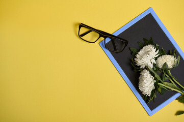 Flat lay of delicate beautiful bouquet of asters autumn flowers and glasses on a blank empty chalkboard with space for text isolated on yellow background