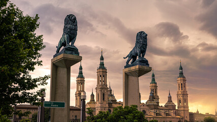 Bronze lions sculpture with the roofs and spires of Zaragoza Cathedral Basilica - obrazy, fototapety, plakaty