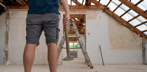 Construction worker with a hammer during the renovation of the attic of a house.