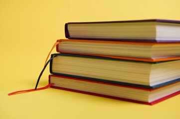 Close-up studio shot of a stack of multicolored books on yellow surface background with copy space...