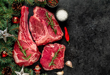 Variety of Christmas Raw Beef Steaks. Ribeye steak, tomahawk, T-bone, with tree and Christmas toys on the stone background with copy space for your text