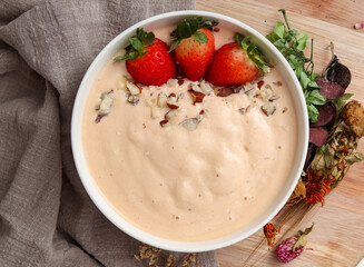 banana, papaya and coconut smoothie accompanied by Strawberries and Brazil nuts, in a white bowl and decorated with dried flowers