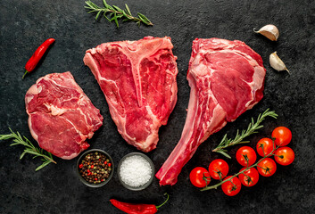 A variety of raw steaks. Ribeye steak, tomahawk, T-bone, on a stone background