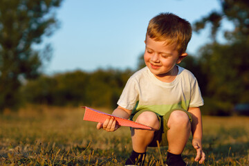 Small blonde caucasian boy three years old playing with paper plane in the field in nature in sunny summer or autumn day growing up childhood growing up carefree concept copy space