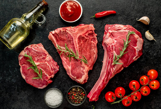 A variety of raw steaks. Ribeye steak, tomahawk, T-bone, on a stone background