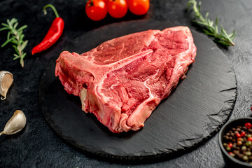 raw T-bone steak with spices ingredients on a stone background