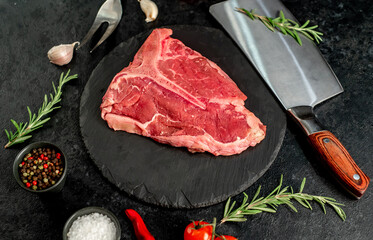 raw T-bone steak with spices ingredients on a stone background