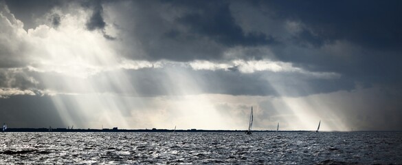 Sailing yacht regatta. Modern sailboat racing through the waves. Dramatic sky with flowing sun rays...