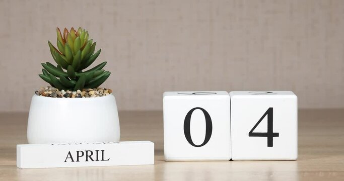 Wooden calendar with an important event for april 4, a woman's hand sets the date on the calendar. Spring season.