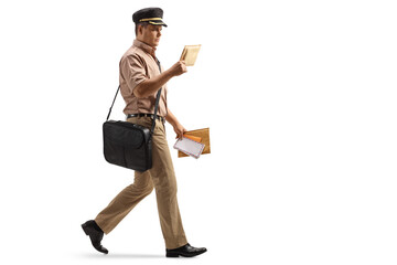 Full length profile shot of a mailman walking and reading a letter - obrazy, fototapety, plakaty