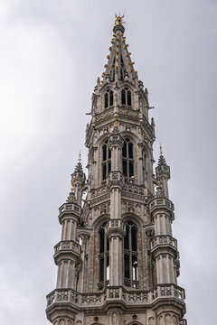 Brussels, Belgium - July 31, 2021: Gray stone top of City Hall spire against gray sky. Golden Saint Michael killing dragon on top.