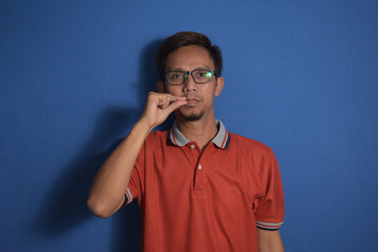 Young asian man over blue background mouth and lips shut as zip with fingers, secret and silent