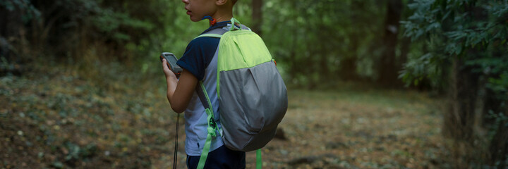 Explorer boy alone at the forest trying to get oriented with a GPS device