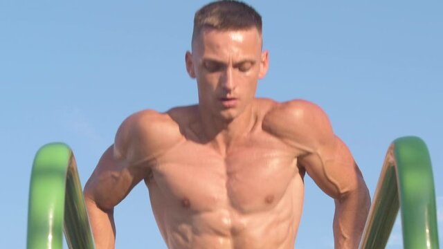 Muscular athletic young man doing pusр ups on parallel bars. Sport and health care concept .