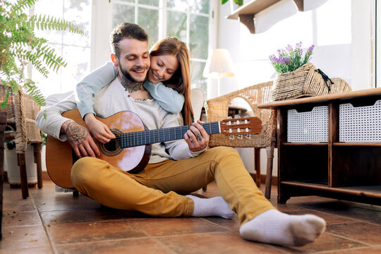 Smiling guitarist playing guitar while interacting with girlfriend at home