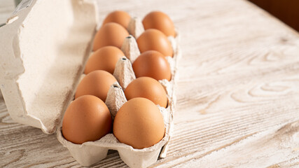 Brown chicken eggs in the box on the table. Package of 10 eggs. Fresh farm egg in carton container on wooden background.