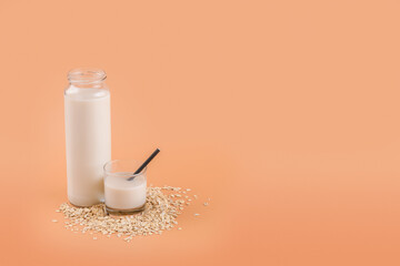 Trendy Vegan non dairy alternative milk. Oat milk in bottle and in a glass on the oat flake on pastel peach color background, copy space