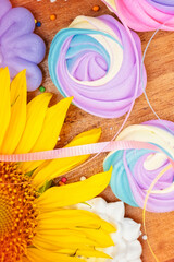 Assorted colorful meringues and sunflowers on a wooden background
