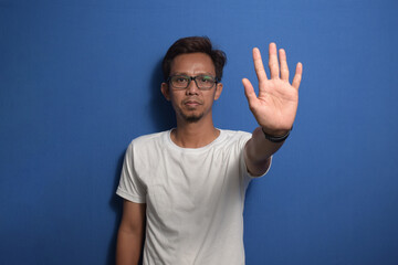 Naklejka premium Young Asian man wearing a white t-shirt over blue background doing stop sing with palm of the hand
