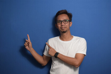 Young Asian man wearing a white t-shirt smiling and pointing with two hands and fingers to the side