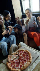 Sporty teenagers with different hairstyles eat pizza sitting on the couch