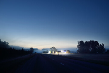 Country highway (asphalt road) in a fog at sunset. Filling station in the background. Moonrise,...