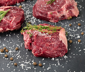 raw piece of beef ribeye with rosemary, thyme on a black table