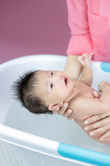 Fototapeta na wymiar Newborn having a bath in basin by mother pink background