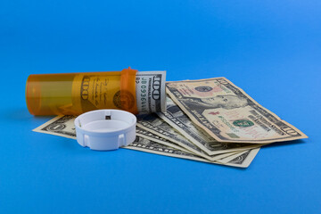Hundred dollar bill and smaller dollar bills with a pill bottle representing the high cost of drug...