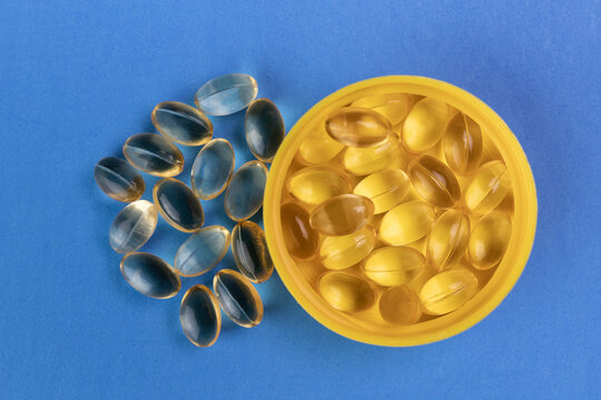 Vitamin D gel pills in a yellow cap and against a blue background. Vitamin D may help in preventing respiratory infections such as COVID-19.