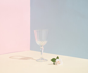 Minimal party life concept. Wine glass and rose on pastel background. Summer scene with pink  flower.