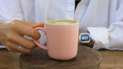Close up of hands pulling towards wooden tray with pink mug matcha tea latte served on it