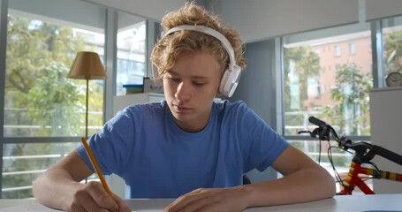 Caucasian teen boy in headphones writing down info during online lesson on laptop at home