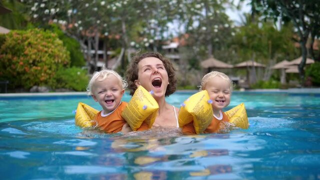  Young White Mom With Her Twins Girls In A Swimming Pool Having Fun. Girls Wearing Inflatable Arm Swimming Ring For Safety