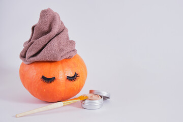 brush, aluminum jar with cosmetic clay face mask and orange pumpkin with towel and false eyelashes on gray background