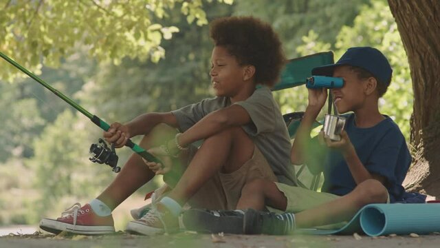 Slowmo shot of cute African American boys spending summer day outdoors in forest, fishing and using binoculars for watching fish and animals